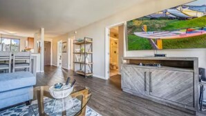 A modern living room with a flat-screen TV, a glass coffee table, a sofa, and a herringbone-patterned cabinet.
