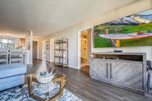 A modern living room with a flat-screen TV, a glass coffee table, a sofa, and a herringbone-patterned cabinet.