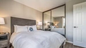 A hotel room with a large bed, a nightstand, a mirror, and a door.