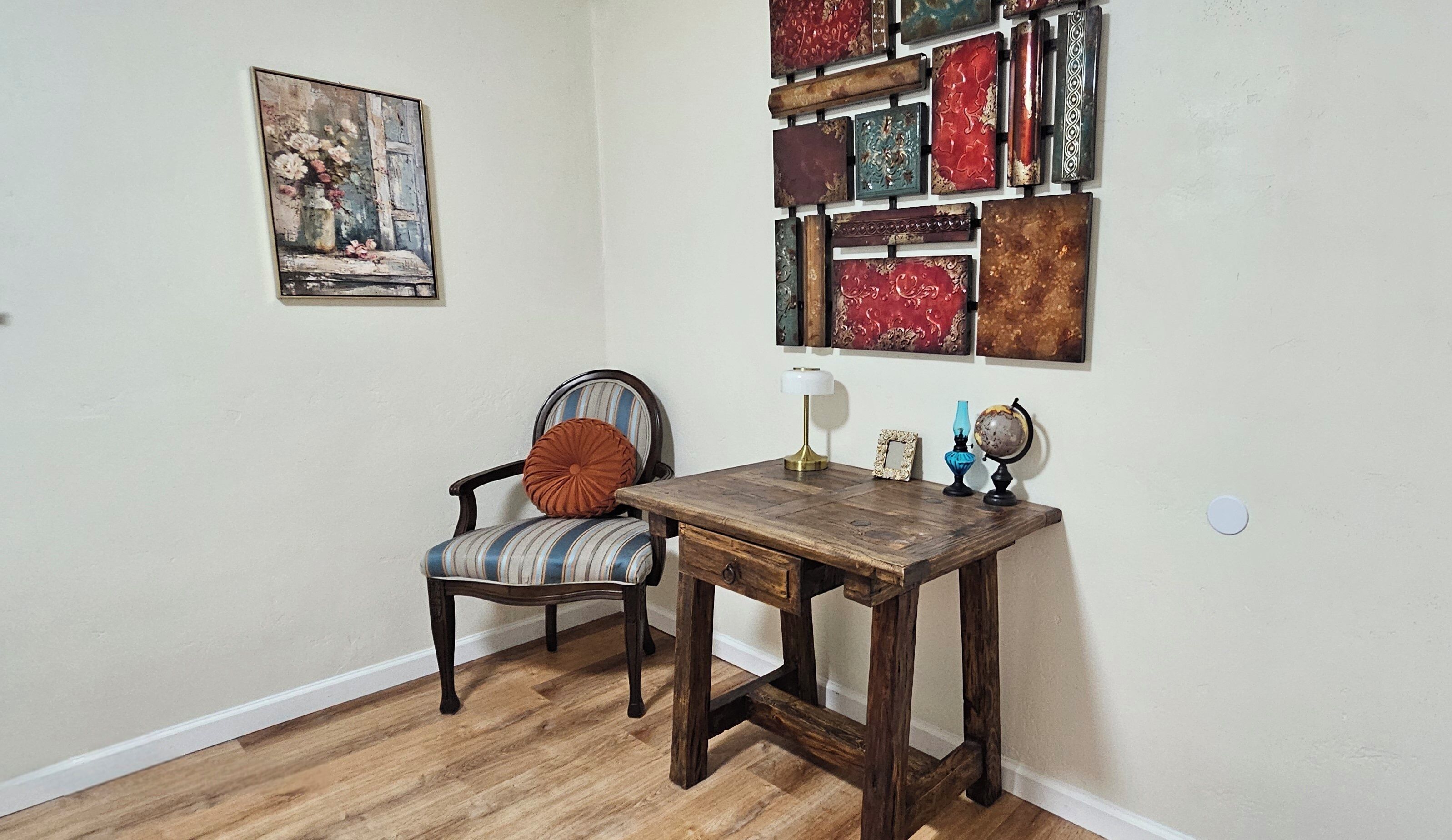 A room with a wooden chair, a small table, a lamp, a globe, and a wall-mounted picture.