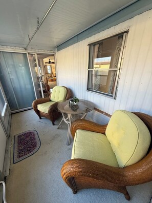 Ein Zimmer mit Korbmöbeln, einem Glastisch und einem Fenster mit gemusterten Vorhängen.