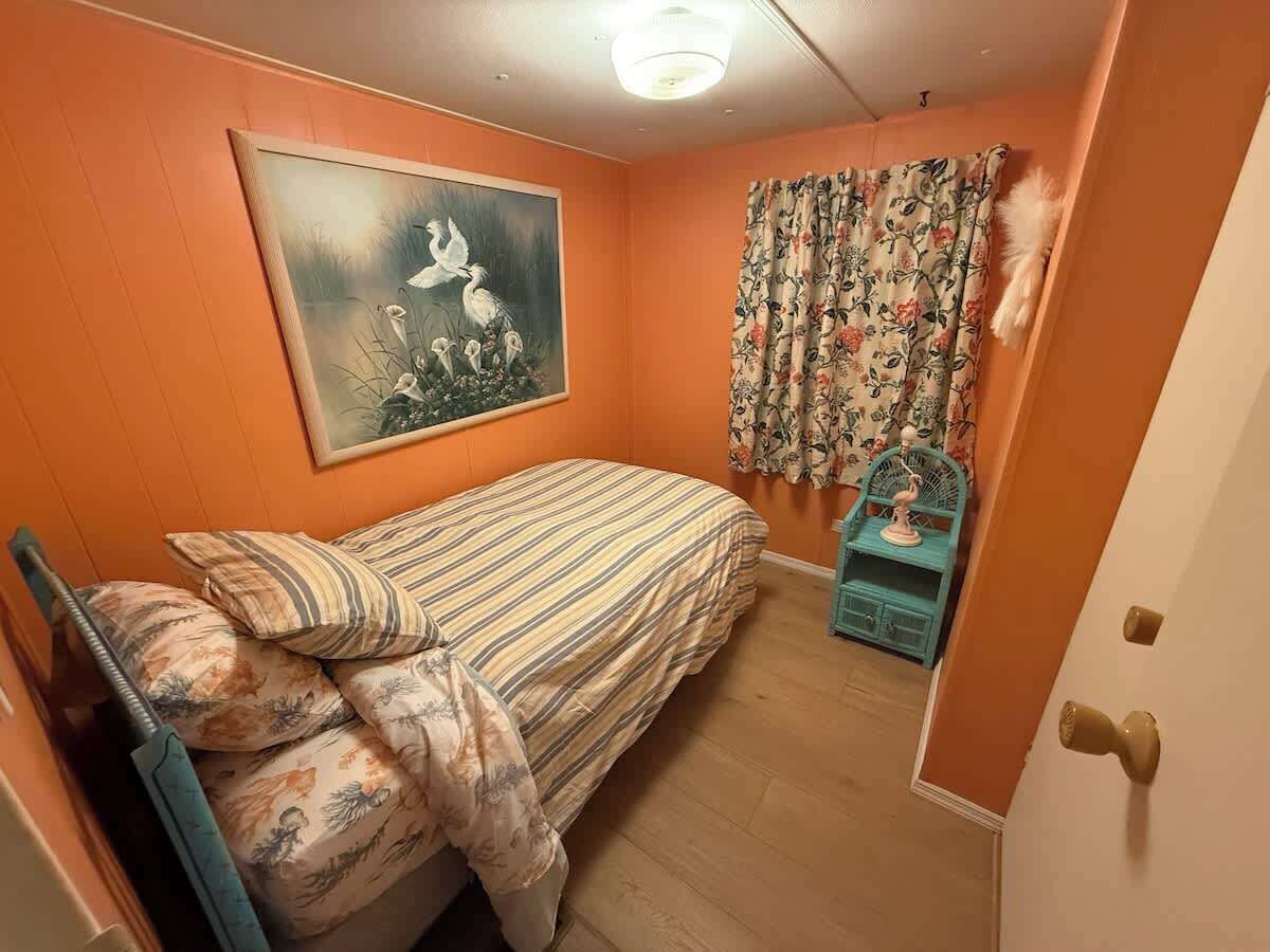 A bedroom with a bed, a painting, curtains, and a small blue cabinet.