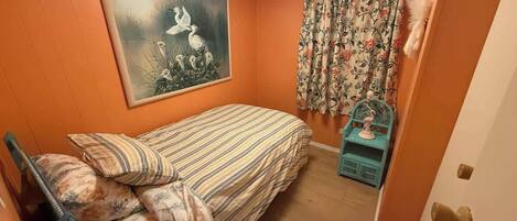 A bedroom with a bed, a painting, curtains, and a small blue cabinet.