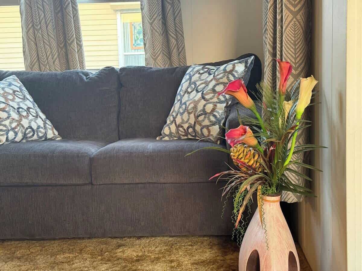 Un canapé gris agrémenté de coussins à motifs, un vase décoratif avec des fleurs et un tapis à texture intéressante.