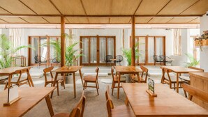 A spacious indoor dining area with wooden tables and chairs, large windows, and potted plants. - Cannella Suites Ubud (Ubud)