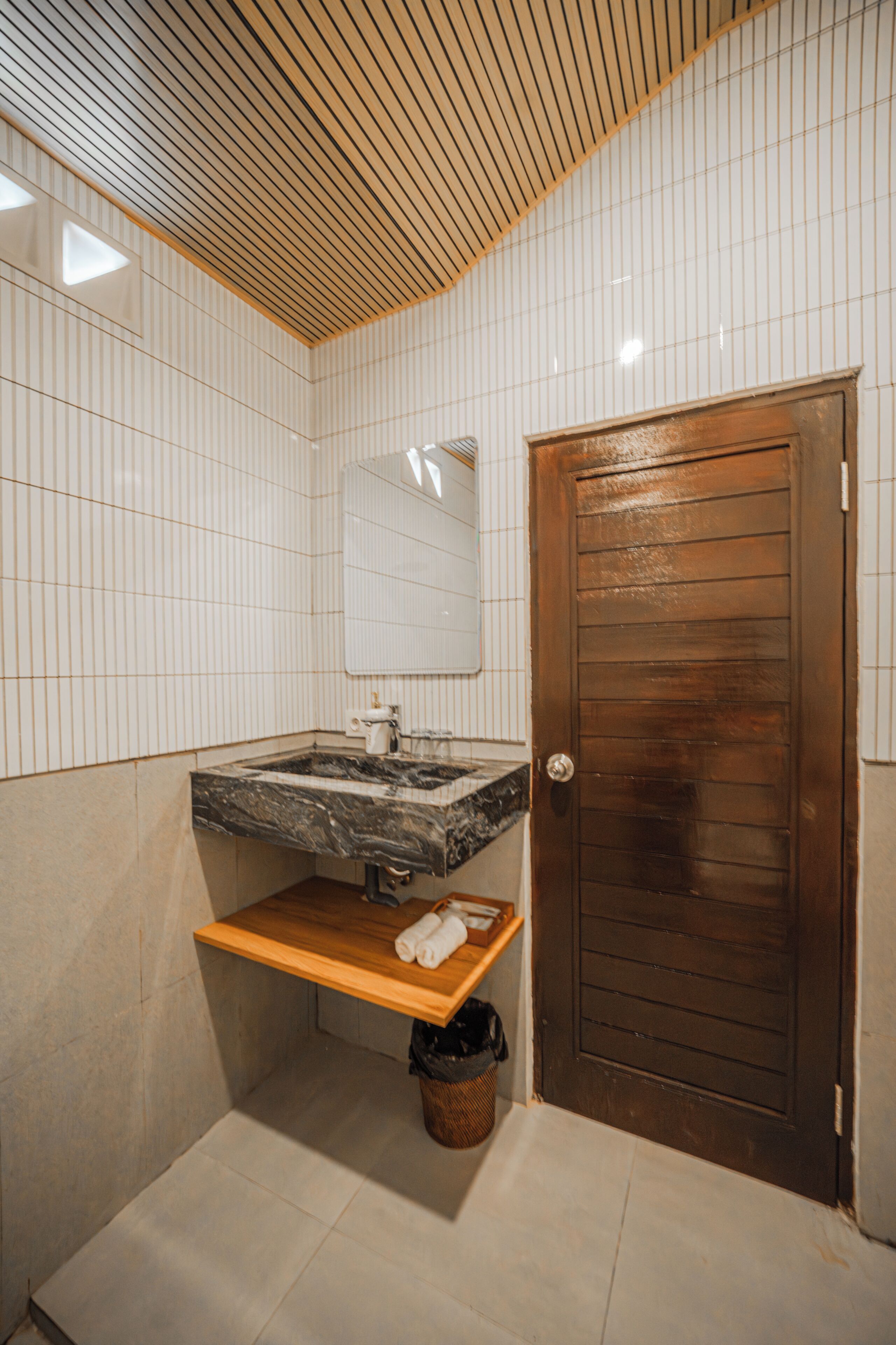 A bathroom with a wooden door, a marble sink, a mirror, and a shelf with towels.
