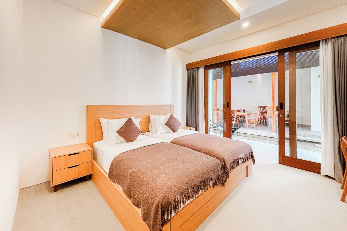Quarto moderno com cama de madeira, mesa de cabeceira e uma grande porta de vidro deslizante para área externa.
