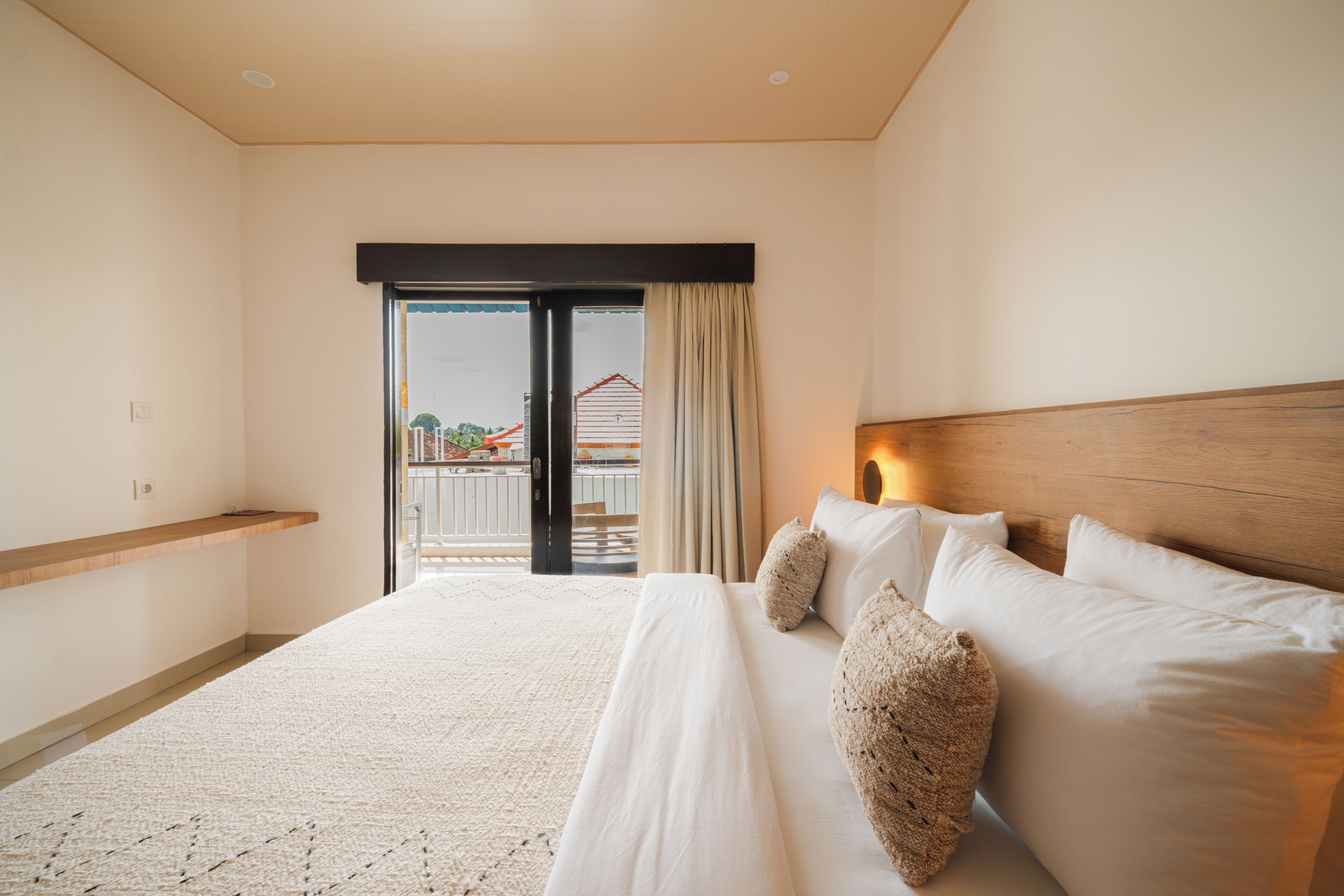 Habitación de hotel con cama, cabecera de madera, balcón con vistas y suelo alfombrado.