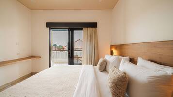 Habitación de hotel con cama, cabecera de madera, balcón con vistas y suelo alfombrado.