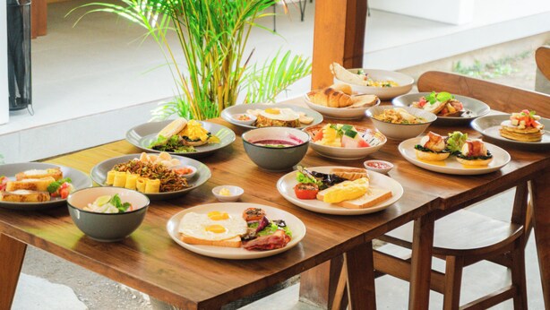 A dining table with various dishes, a potted plant, and wooden chairs. - Cannella Suites Ubud (Ubud)