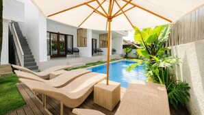 A modern outdoor pool area with lounge chairs and a large umbrella. - Cannella Suites Ubud (Ubud)