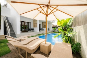 A modern outdoor pool area with lounge chairs and a large umbrella.