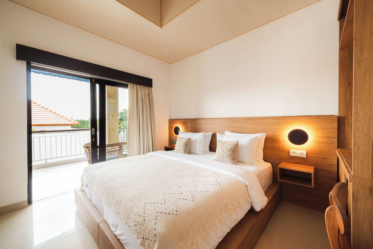 Quarto moderno com uma cama grande, cabeceira de madeira, abajures e uma varanda com vista.