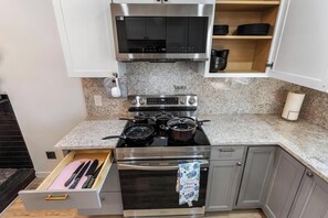 A kitchen with a stove, oven, microwave, and a drawer with utensils.