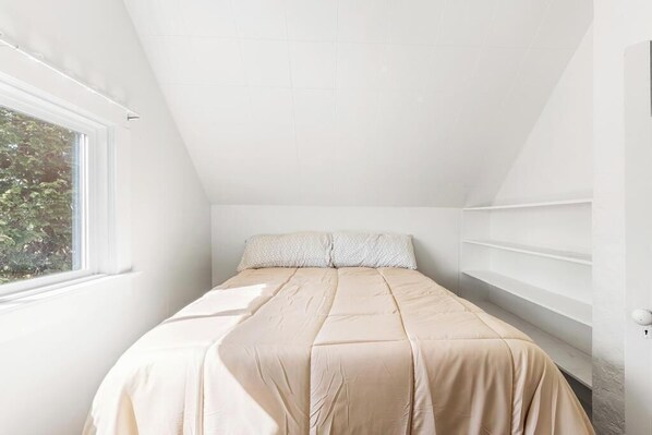 A bedroom with a sloped ceiling, a bed with a beige bedspread, a window, and built-in shelving. - Sunset Farmhouse Retreat in Skagit Valley (Burlington)