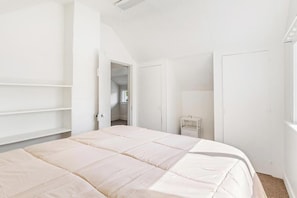 A bedroom with a bed, a wardrobe, a nightstand, and a door leading to another room.