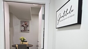 A hallway leading to a dining area with a table and chairs, a framed inspirational quote on the wall, and a door with a handle. - Xquisithomes: More than a stay, it's an experience (Saskatoon)