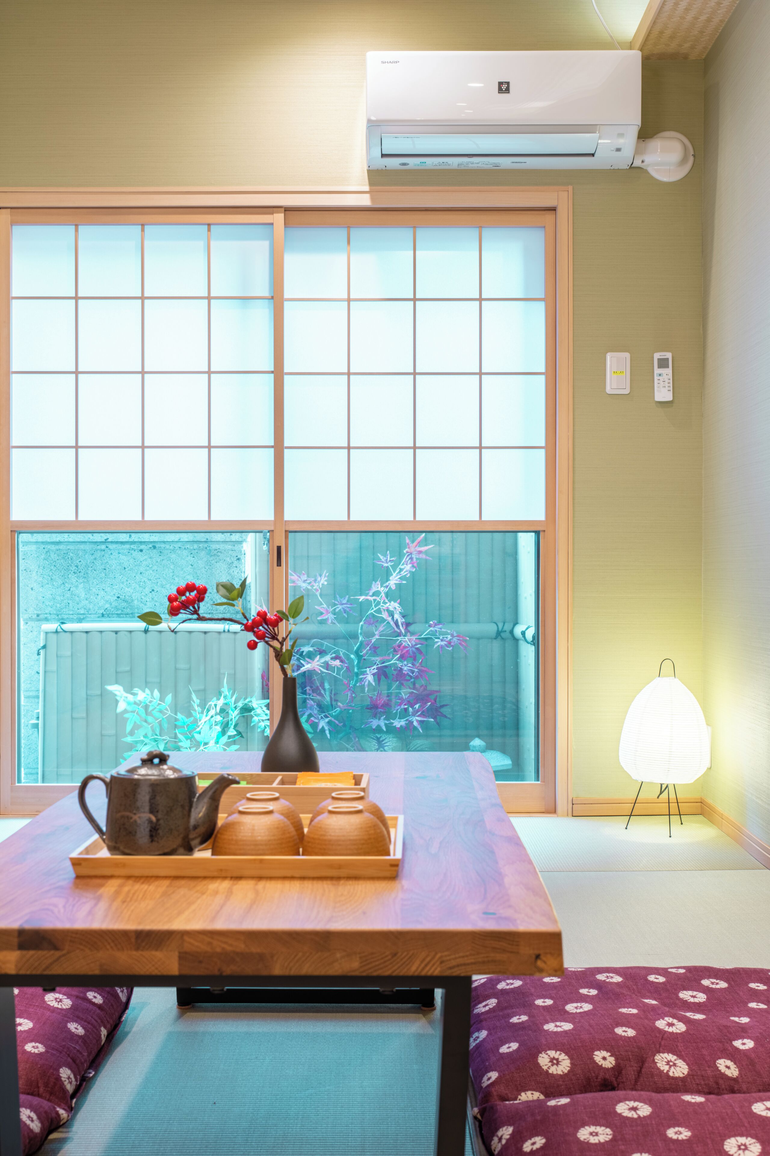 A traditional Japanese room with tatami flooring, a low table with a vase and teapots, and a sliding shoji screen.