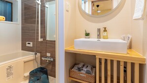 Un baño con bañera, ducha, lavabo con espejo y estante con cesta.