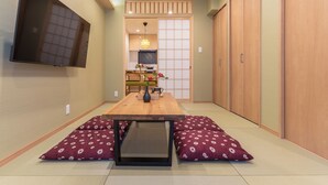 Una habitación japonesa tradicional con suelo de tatami, una mesa baja, cojines, televisión y puertas correderas.