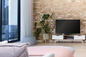 Sala de estar com parede de tijolos, janela ampla, televisão de tela plana, planta em vaso e sofá moderno.