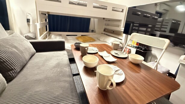 A bunk bed with a desk, a couch, and a table with mugs and plates. - GrAce Room IKEBUKURO (Tokyo)