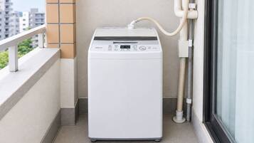 Máquina de lavar roupa compacta e branca numa varanda, com vista para a cidade.