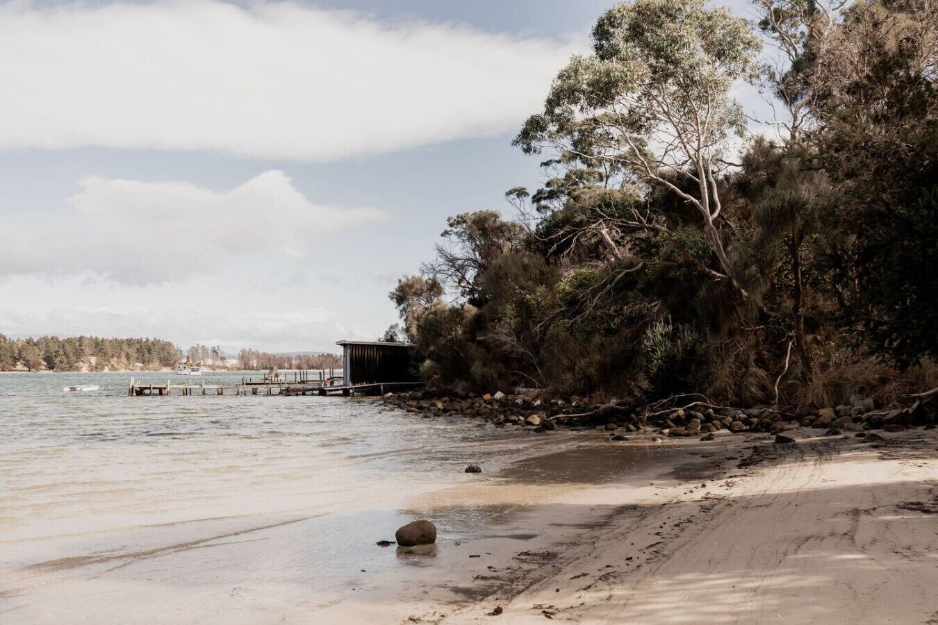Une plage avec une structure en bois, des arbres et une étendue d’eau calme.