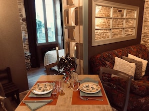 Un comedor con una mesa dispuesta para dos, un centro de mesa con velas y vistas al exterior a través de una ventana.
