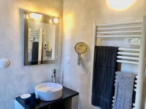 A bathroom with a round sink, a mirror with lights, a towel rack, and a wall-mounted heater. - Les Fleurs De Lys, Suites&Appart , Entrée et Terrasse Privée Proche de la Mer (Saint-Georges-d'Oléron)