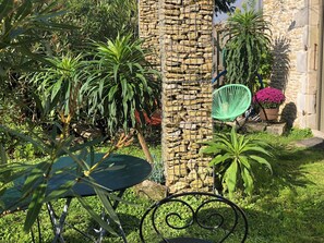 A garden with a stone wall, a green chair, and a table. - Les Fleurs De Lys, Suites&Appart , Entrée et Terrasse Privée Proche de la Mer (Saint-Georges-d'Oléron)