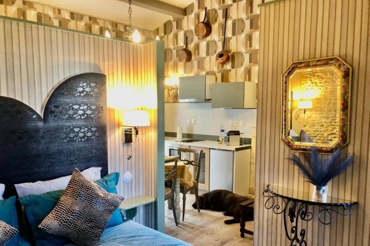Une chambre avec un lit, une chaise, un chien, une table de chevet et un coin cuisine avec des placards et un évier.