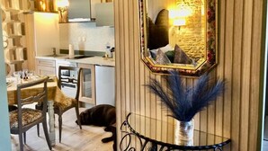 A dining area with a table set for two, a mirror with a decorative frame, and a vase with feathers. - Les Fleurs De Lys, Suites&Appart , Entrée et Terrasse Privée Proche de la Mer (Saint-Georges-d'Oléron)
