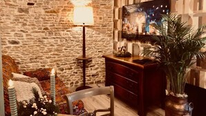 A cozy room with a stone wall, a flat-screen TV, a wooden dresser, and a potted plant. - Les Fleurs De Lys, Suites&Appart , Entrée et Terrasse Privée Proche de la Mer (Saint-Georges-d'Oléron)