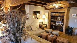 Ein gemütliches Wohnzimmer mit einer Sofagarnitur, einer großen Topfpflanze und einem Holzbücherregal.