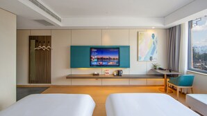 A hotel room with two beds, a TV, a desk, a chair, a window with a city view, and a coat rack. - ZMAX HOTELS Fenghuang Ancient Town (Xiangxi)