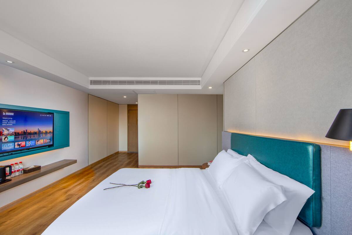 Una habitación de hotel moderna con una cama grande, un televisor montado en la pared y piso de madera.