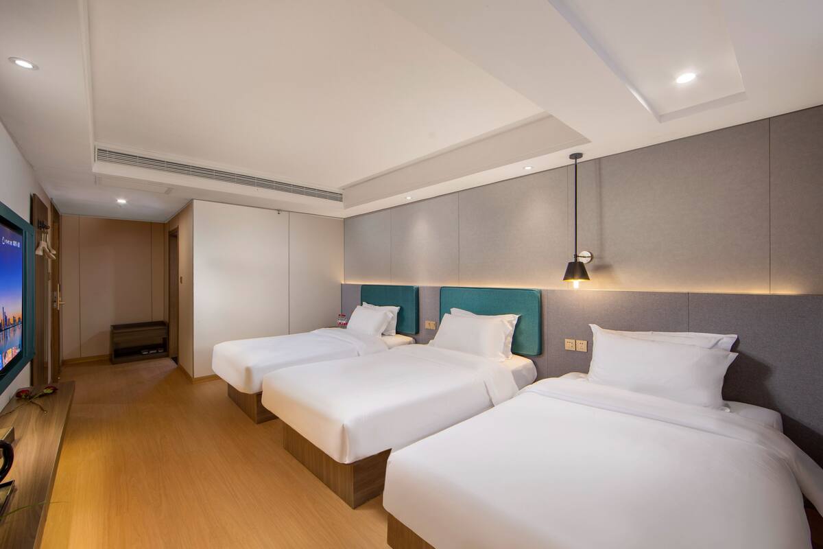Habitación de hotel con tres camas, televisión y un diseño moderno.