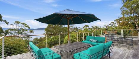Una terraza al aire libre con mesa y sillas, un paraguas grande y vistas al agua.