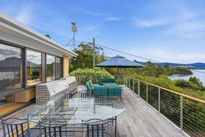 Una terraza con una mesa y sillas de vidrio, una parrilla y vistas a un lago.