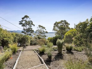 A garden with a gravel path leading to a body of water, surrounded by various shrubs and trees. - Beach house 150 m from Coningham Beach, bay views, 10 min to the Bruny ferry (Coningham)