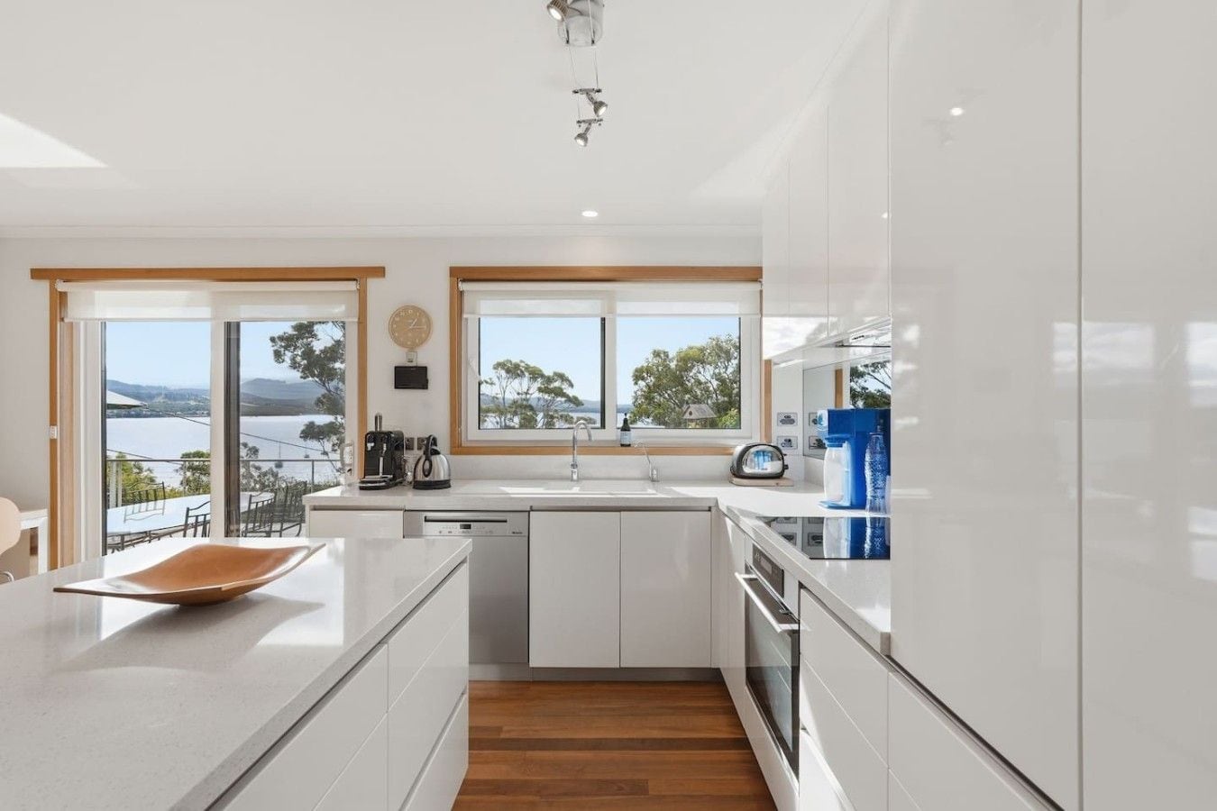 A modern kitchen with a large island, a view of the outdoors, and a wooden floor.