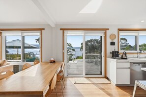 Cocina moderna con vista al mar, zona de comedor con mesa de madera y puerta corrediza de vidrio que da a una terraza exterior.