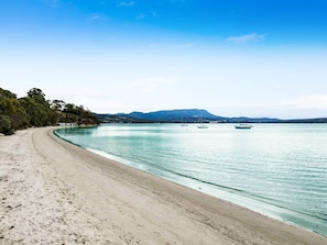 Ein Strand mit klarem türkisblauem Wasser, einem sandigen Ufer und Booten in der Ferne.