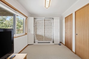 Ein Zimmer mit Fernseher, Fenster, weißem Heizkörper und Holztür.