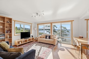 A modern living room with a television, sofa, and dining area. - Beach house 150 m from Coningham Beach, bay views, 10 min to the Bruny ferry (Coningham)
