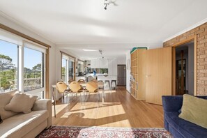 A spacious living area with a dining set, a sofa, and a view through large windows.