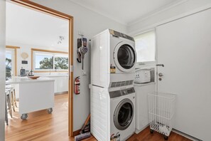 A laundry room with two stacked washing machines, a fire extinguisher, and a white laundry basket.