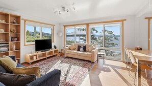 Ett rymligt vardagsrum med en stor TV, en soffa, ett soffbord och en matplats med utsikt över vattnet.