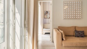 Et værelse med en beige sofa, en pude med et mønster, et indrammet kunstværk og en geometrisk dekoration på væggen.